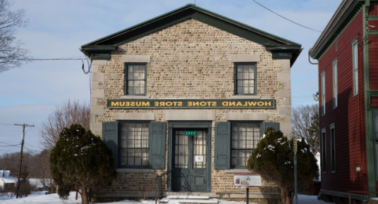 An old brick building with blue accents is labeled Howland Stone Store Museum.